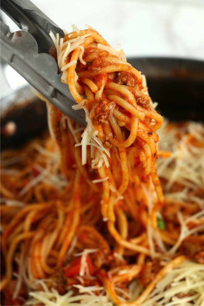 Closeup shot of tongs holding school cafeteria spagehtti