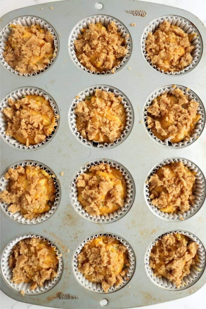 Overhead shot of unbaked pumpkin zucchini muffins with crumble topping in muffin tin