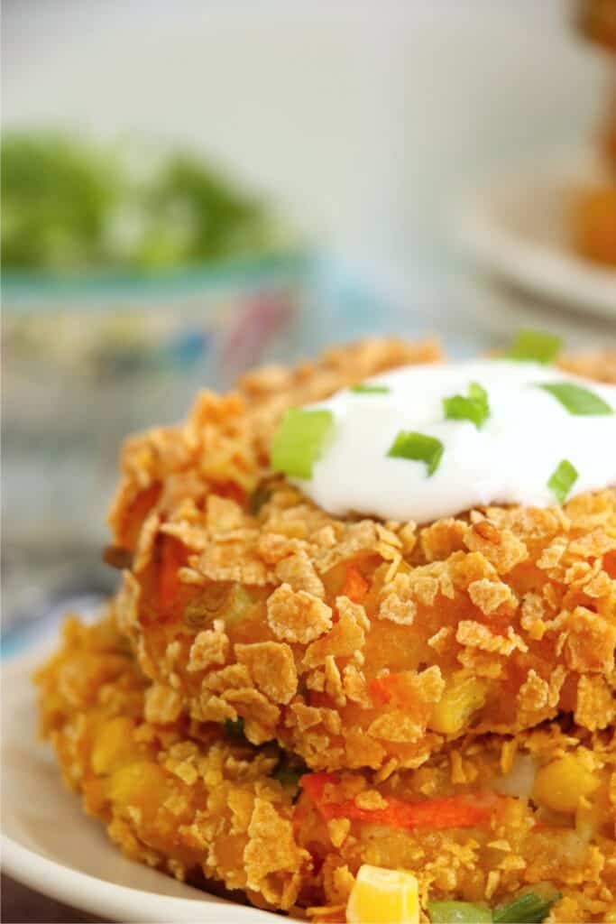 Closeup shot of two mashed potato and vegetable patties stacked atop one another on plate and topped with sour cream.