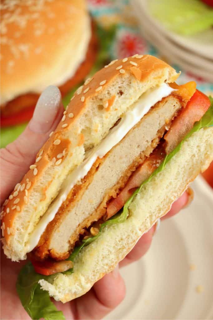Closeup shot of hand holding half an air fryer chicken patty sandwich with lettuce, tomato, and mayo.