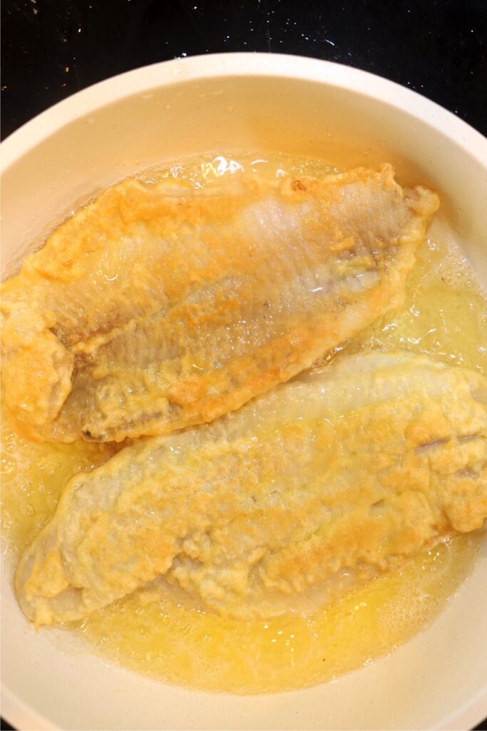 Closeup overhead shot of golden brown catfish frying in skillet.
