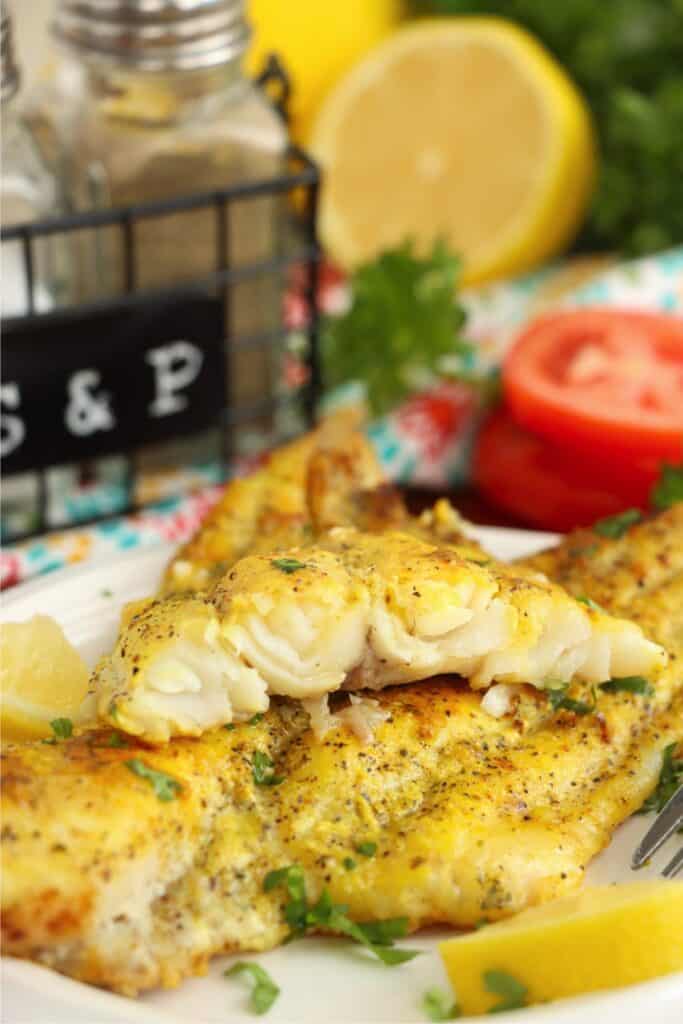 Closeup shot of pan fried catfish filets stacked atop one another on plate with top filet cut in half. 