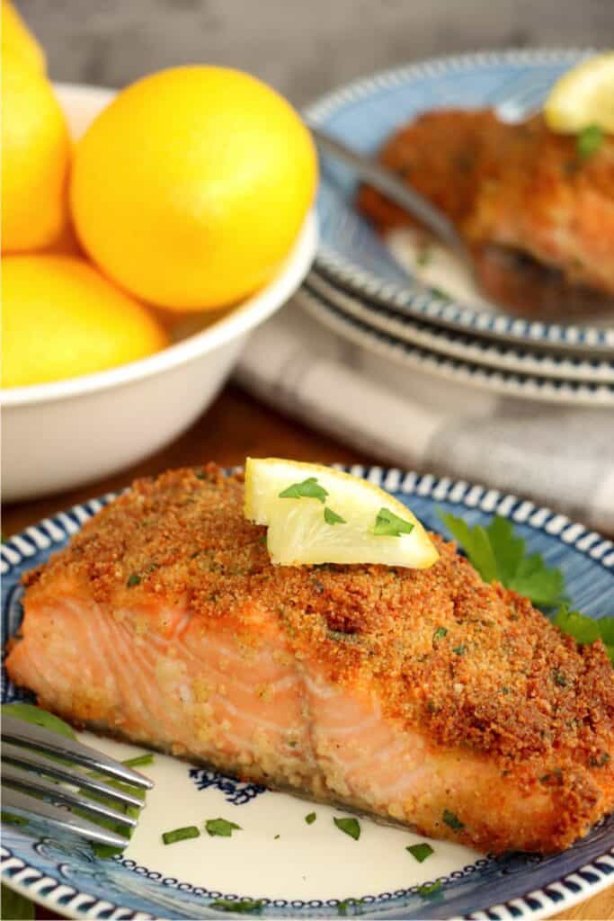 Closeup shot of herb crusted salmon fillet toppoed with lemon wedge on plate. 