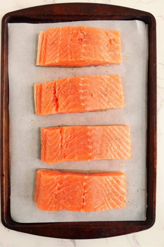 Overhead shot of raw salmon filets on baking sheet lined with parchment paper. 